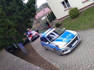 na zdjęciu widać jak policyjny radiowóz wyjeżdża z posesji DPS w Wydminach, za radiowozem jedzie samochód OSP w Wydminach