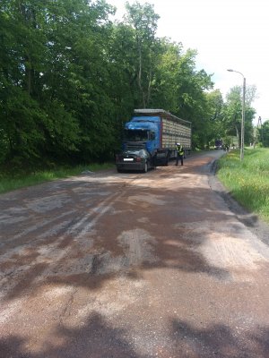 na zdjęciu znajduje się  jezdnia gdzie na łuku drogi w prawo stoją dwa pojazdy - osobowy przed ciężarowym, obok których stoi policjant w odblaskowej kamizelce