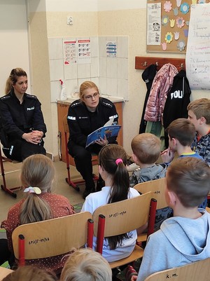 na zdjęciu znajdują się policjantki gdzie jedna z nich czyta dzieciom książeczkę
