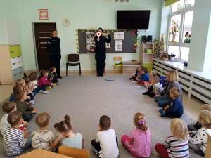 na zdjęciu znajdują się policjantki w sali Przedszkola gdzie pokazują dzieciom tarczę do zatrzymywania, przed nimi siedzi grupa dzieci