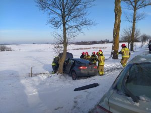 na zdjęciu znajduje się samochód osobowy przylgnięty drzwiami kierowcy do przydrożnego ośnieżonego rowu, przy samochodzie znajduje się grupa strażaków