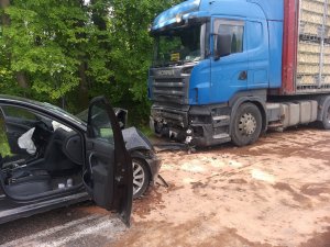 na zdjęciu z lewej strony znajduje się część przednia samochodu osobowego z uszkodzeniami a przed nim na jezdni znajduje się przód samochodu ciężarowego