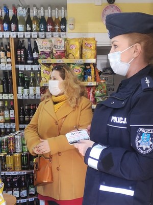na obrazku znajduje się policjantka wewnątrz sklepu trzymająca w ręku ulotkę a obok niej kobieta
