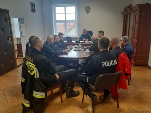 na zdjęciu znajdują się policjanci oraz przedstawiciel Straży Pożarnej, MOPRu siedzący przy stole w pokoju Komendy Policji