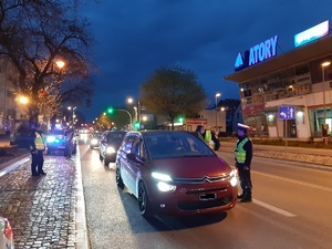na zdjęciu widoczny jest czerwony pojazd zatrzymany do kontroli drogowej na ulicy w Giżycku. obok stoją umundurowani policjanci ruchu drogowego, którzy sprawdzają stan trzeźwości kierwocy