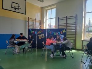 na zdjęciu widać uczniów siedzących przy stolikach i pracujących nad zadaniem konkursowym