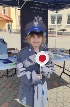 na zdjęciu znajduje się dziewczynka ubrana w policyjny mundur ze znakiem do zatrzymywania pojazdów stop