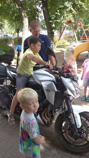 na zdjęciu znajduje się motocykl policyjny obok którego stoi policjant, na motocyklu siedzi chłopiec