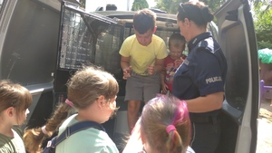 na zdjęciu znajduje się policjantka, która pomaga dziecku wsiąść do radiowozu