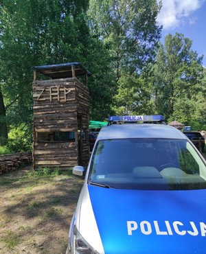 na zdjęciu znajduje się radiowóz policyjny na tle drewnianej baszty z napisem zrobionym z drewna ZHP