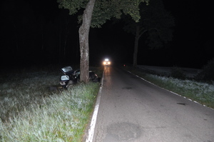 na zdjęciu znajduje się ulica po lewej stronie stoi drzewo za który znajduje się wbity w nie samochód